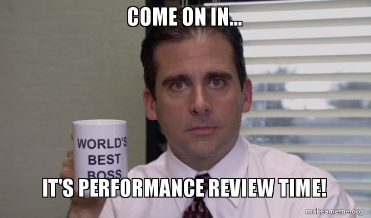 Michael Scott of The Office holds up a "world's best boss" mug. The text says Come on in... it's performance review time. 