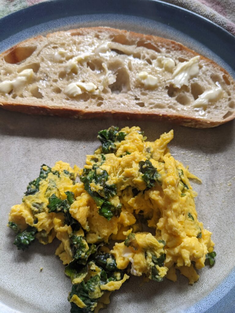 a pile of scrambled eggs with kale and toast with butter